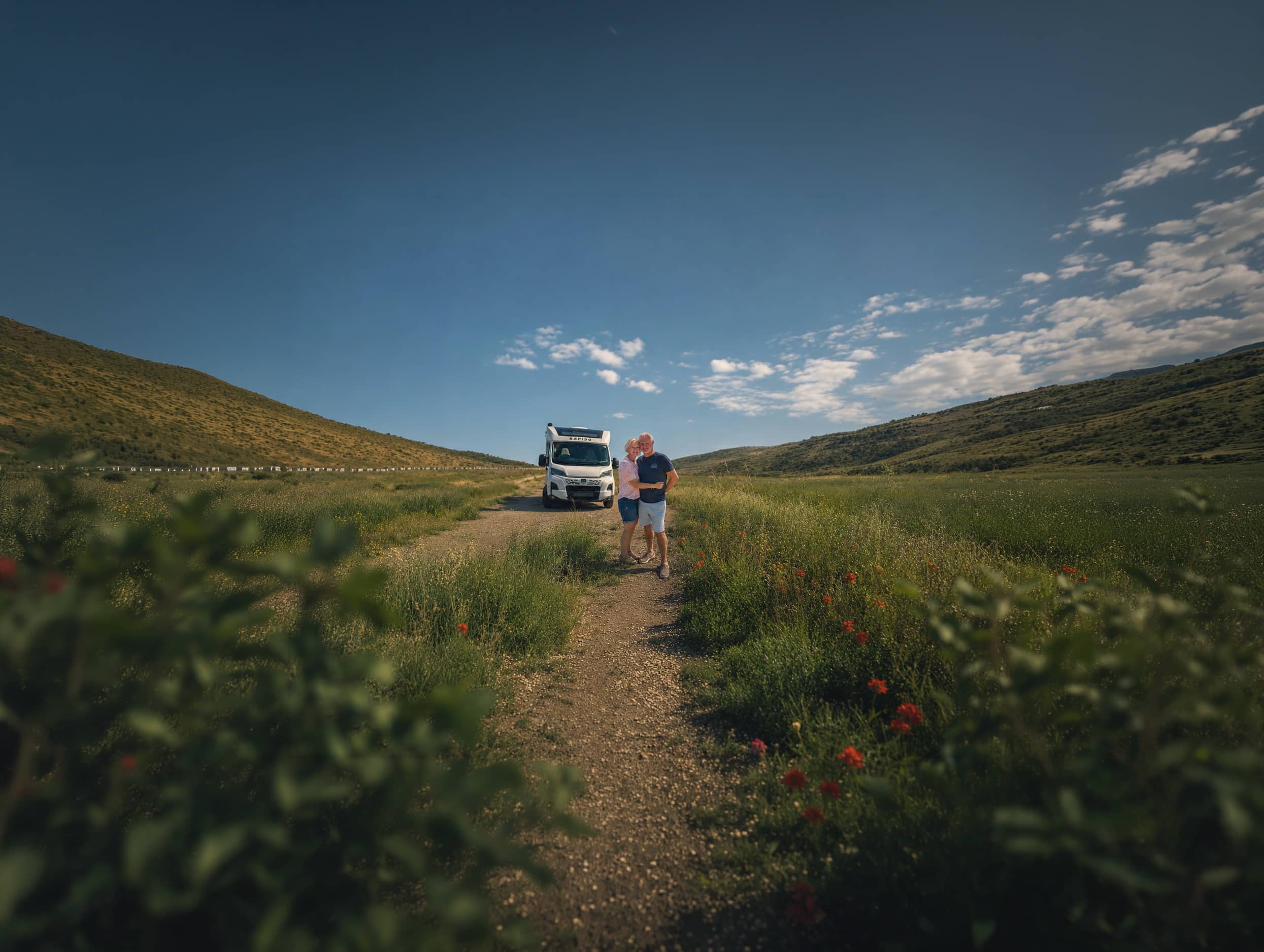 A couple standing beside their RV on a track through green rolling hills
